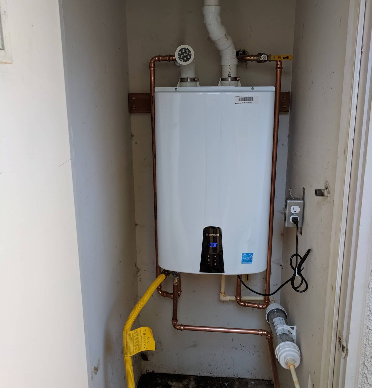 Wall-mounted Navien tankless water heater in an indoor utility closet